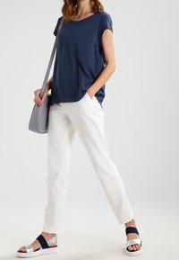 Námořnické texturované tričko s krátkým rukávem, bílé rovné kalhoty, stříbrné a námořnické sandály na pásky a světle šedá crossbody taška.