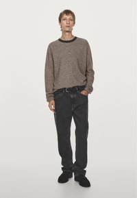 Gray knit sweater with black trim, dark loose-fitting jeans, and black shoes. Standing pose, hands relaxed. Simple, casual clothing.