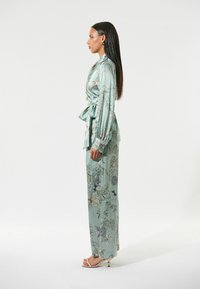 Bloemmotieven, lichtblauwe satijnen blouse en broek met wijde pijpen. Kenmerken zijn een wikkelontwerp, lange mouwen en een stoffen strik in de taille.