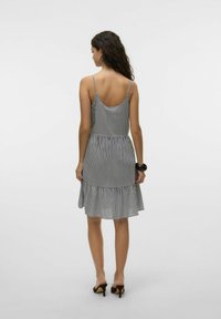 Pasiasta sukienka na ramiączkach, z dopasowanym górą i rozkloszowanym dołem wykończonym falbanką. Materiał wydaje się lekki; kolorystyka jest czarno-biała.