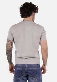 Camiseta de manga corta ajustada de color gris claro con un patrón texturizado, cuello redondo y bordes acanalados. Combinada con jeans de mezclilla azules.