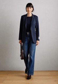 Navy pinstriped blazer with a single button, paired with high-waisted blue jeans. Brown leather handbag and shoes complete the look.