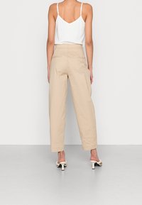 Beige högmidjade byxor i lätt tyg med avslappnad passform och sidofickor, ihop med en vit tanktop och klacksandaler.