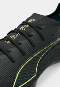 Crampon de football noir avec surface texturée, accents verts le long des côtés et lacets contrastants. Présente un design épuré pour la performance.