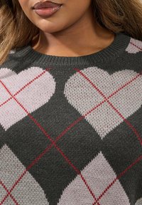 Grauer Strickpullover mit einem Herzmuster in Pink, umrandet mit Rot, und einem gerippten runden Halsausschnitt. Weiche Textur mit einem gemütlichen Aussehen.