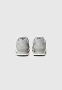 Pelēki sporta apavi ar zamšāda un tīkla augšdaļu, kuriem ir bieza baltā starpsole un melna gumijas zole. "New Balance" logo uz papēža.
