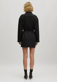 Schwarzes, kurzes Kleid mit langen Ärmeln, lockerer Passform, tailliert und mit kontrastierendem weißen Kragen. Verfügt über glattes, glänzendes Material und minimalistisches Design.