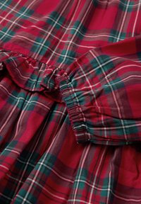 Rood en groen geruit stof met witte strepen, voorzien van gatheringmouwen en een gekreukt randje. Zachte textuur en gladde afwerking.
