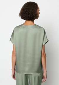 Top corto in satin a maniche corte verde chiaro, con scollatura rotonda e una vestibilità ampia. Tessuto liscio con un design minimalista complessivo.