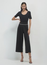 Tutina nera con maniche corte, scollatura a barca, design a gamba larga e vita impreziosita. Tessuto liscio con un aspetto elegante e dettagli minimi.