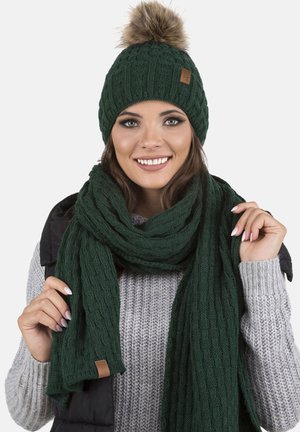Groene gebreide beanie met een nep bont pompon, gecombineerd met een bijpassende gestructureerde sjaal. De muts heeft een klein leren logo-label.