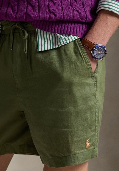 Λινά σορτς σε ελιά πράσινο με κορδόνι στη μέση, σε συνδυασμό με ριγέ πουκάμισο και καφέ δερμάτινο ρολόι. Διαθέτει ένα μικρό κεντημένο λογότυπο.