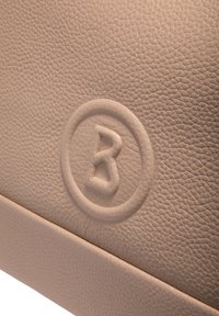 Sac en cuir beige texturé avec un logo circulaire en creux présentant une lettre 'B' stylisée. Finition lisse avec un motif de grain apparent.