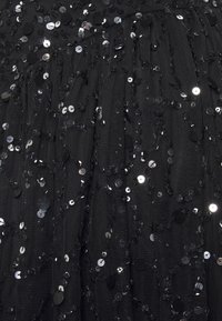 Tissu noir texturé avec des rangées de sequins noirs brillants qui se chevauchent, de tailles variées, créant un effet de surface visuel dynamique.