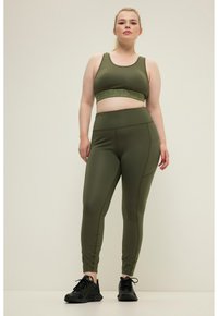 Olijfgroen sportset bestaande uit een aansluitende sportbeha en high-waisted leggings met een gestructureerde tailleband en naaddetails.