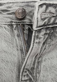 Grijs denim jeans met een metalen knop met het label "AUTHENTIC," een ritssluitting en een getextureerd oppervlakdetail.