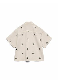 Camisa beige de manga corta con cuello, que presenta pequeños patrones geométricos en forma de diamante en color negro esparcidos por la parte de atrás y las mangas.