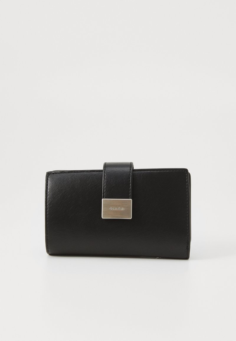 Billetera de piel negra con textura suave, forma rectangular y detalles de cierre en tono plateado. La parte frontal presenta una pequeña placa con el logo.