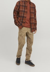 Kostkovaná košile v hnědé a námořnické barvě, dlouhé rukávy, spojená s tričkem v rezavé barvě a béžovými cargo kalhotami, doplněná o námořnické tenisky.