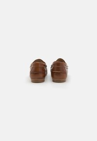 Brune lærloafers med en glat tekstur, rund hæl og tvillinge spænde accenter på hver side. Gummisåler giver fleksibilitet.