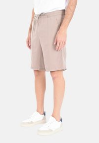 Pantaloni corti beige realizzati in tessuto leggero, con una vita elastica e cordoncino. Abbinati a sneakers bianche con dettagli blu navy.