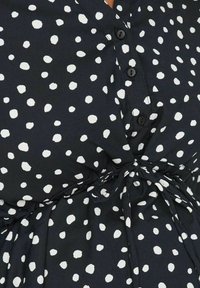 Abito nero con pois bianchi, dotato di chiusura a bottoni e vita legata. Il tessuto ha una texture liscia e leggera.
