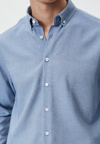 Lichtblauw button-up shirt van zachte katoen, met een klassieke kraag, witte knopen en een gladde textuur met een lichte glans.