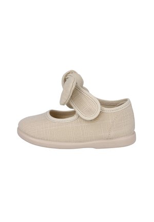 Zapato para niño pequeño de tela beige con punta redondeada, una correa de velcro y un nudo decorativo en la correa, mostrado de lado.
