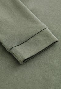 Groene katoenen sweatermouw met een geribde manchette. De stof heeft een zachte textuur met subtiele stiknaden langs de zoom.