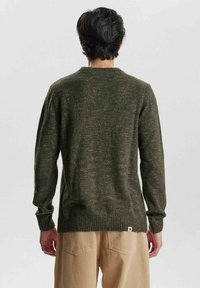Maglione lavorato a maglia di colore verde scuro con una texture mélange. Presenta un orlo e polsini a coste, un collo rotondo e una piccola etichetta con logo nella parte inferiore.