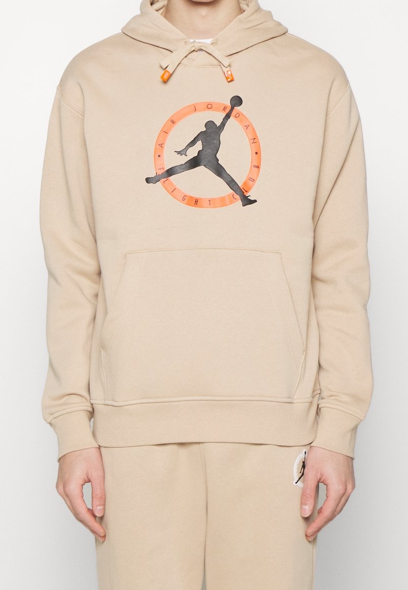 Sudadera con capucha beige con bolsillo tipo canguro en la parte delantera, con un logotipo negro de la silueta de Air Jordan rodeado por un gráfico naranja. Capucha ajustable con cordón.