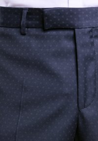 Pantaloni da abito blu navy con sottili motivi a quadri, tessuto strutturato, vestibilità su misura, passanti per cintura visibili e dettaglio della tasca laterale.