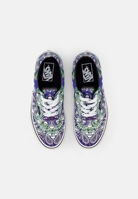 Färgglada Vans-sneakers med ett paisleymönster i lila, grönt och vitt, med vita snörningar och en svart innersula som visar Vans-logotypen.