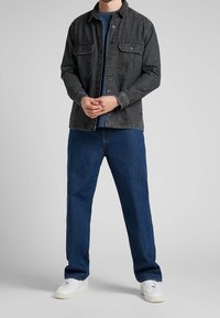 Tmavěmodrá džínová bunda s dvěma náprsními kapsami, pod ní pevná modrá košile, kombinovaná s modrými rovnými džíny a bílými teniskami.