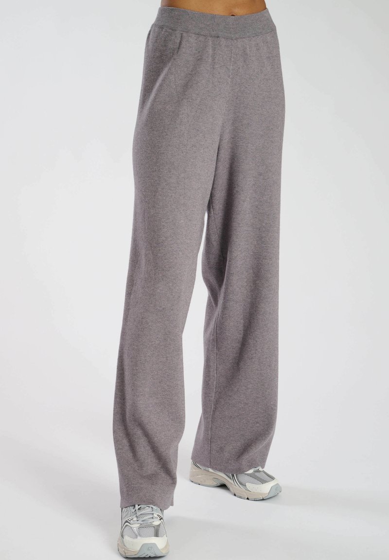 Grå vida sweatpants med mjuk textur, elastisk midja och avslappnad passform, parat med ljusa träningsskor.