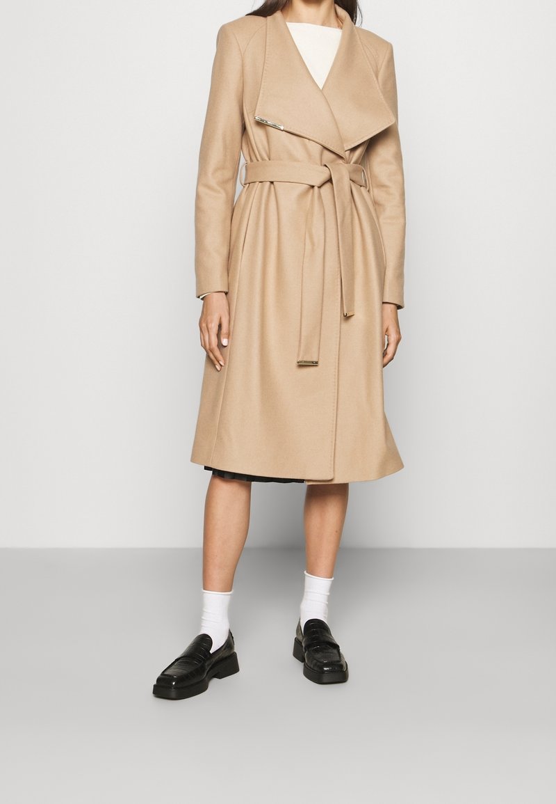 Beige uldblandet trenchcoat med en omslag design, lange ærmer og bælte i taljen. Har en bred revers og subtile detaljer i guldfarvet hardware.