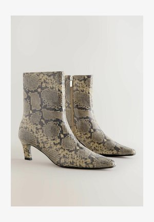 Kígyóbőr mintás bokacsizma hegyes orral, alacsony sarokkal és oldalsó cipzárral. Az anyag texturált, fényes felületű, semleges árnyalatokban.