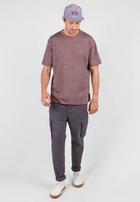 T-shirt texturé bordeaux avec poche poitrine, associé à un pantalon cargo gris avec poches latérales et des sneakers blanches. Casquette à motif violet.