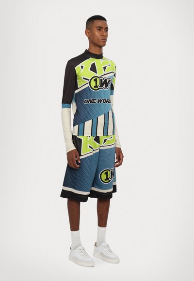 Athletic outfit featuring a long-sleeve graphic top in black, green, blue, and white; matching blue shorts with geometric patterns. White sneakers.