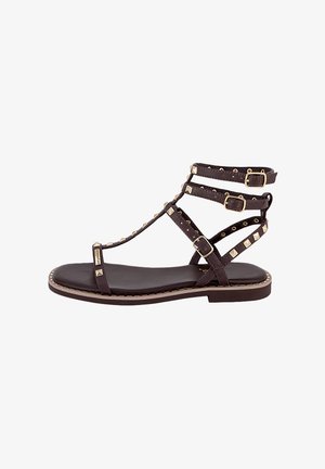 Sandalo piatto nero con molteplici sottili cinturini, borchie color oro e tre fibbie regolabili intorno alla caviglia e al piede.