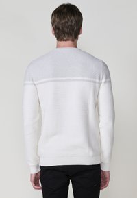 Witte textuurtrui met geribd breipatroon, effen kleur, ronde hals en aansluitende manchetten, gecombineerd met zwarte broek.