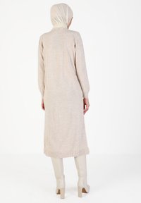 Beige gestricktes langes Kleid mit langen Ärmeln, gerippten Manschetten und einer geraden Silhouette. Kombiniert mit glänzenden kniehohen Stiefeln.