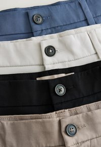 Quatre pantalons pliés en bleu, blanc, noir et beige, chacun avec un bouton visible et une passants de ceinture le long de la ceinture.