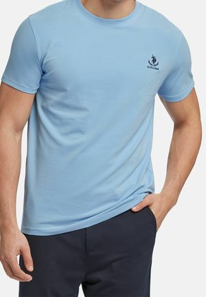 Jasnoniebieska bawełniana koszulka z okrągłym dekoltem, krótkimi rękawami i małym wyszytym logo na piersi. Miękka, gładka tekstura.