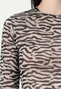 Transparante long-sleeve top met een zebra-strepenpatroon in zwart op een lichtbeige achtergrond, met een ronde hals en een zachte textuur.