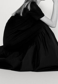Schwarzes Baumwiderkleid mit lockerem Schnitt, ausgestattet mit einem gerafften Saum und kurzen Ärmeln, das sanft über den Körper fällt.