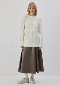 Pull crème douillet à motifs texturés, associé à une longue jupe en satin marron. Accessoires : chaussettes blanches et baskets décontractées.