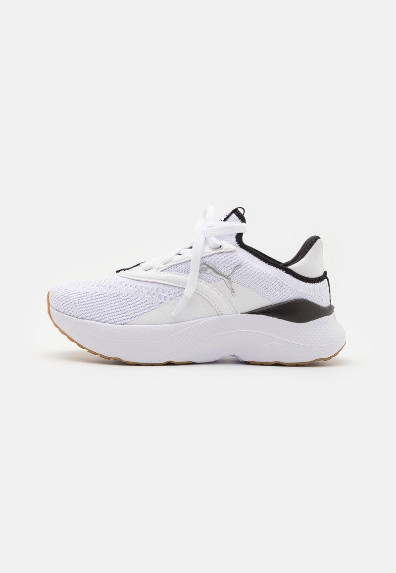Chaussure de sport blanche avec tige en maille, accents noirs et semelle en caoutchouc épaisse. Présente des lacets traditionnels et des zones texturées pour un meilleur soutien.