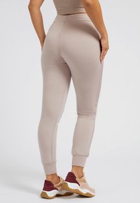 Helle beige Jogginghosen mit einer taillierten Passform, elastischem Bund, schmal zulaufenden Beinen und kontrastierenden Seitestreifen; kombiniert mit mehrfarbigen Sneakern.