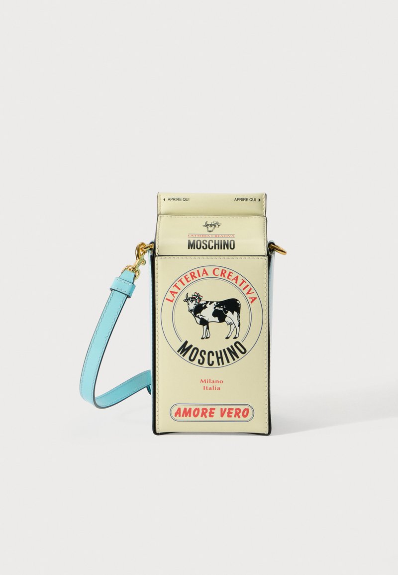 Moschino piena kartona formā veidota rokassomiņa krēmkrāsā ar melniem akcentiem, ar zilu siksnu un drukātu govs logotipu, kuras augstums ir aptuveni 25 cm.